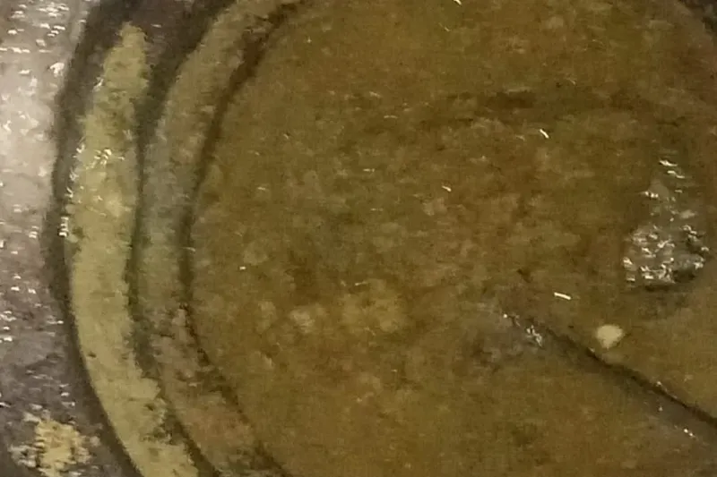 Caixa de gordura redonda aberta, com uma camada de gordura amarelada sobre a água